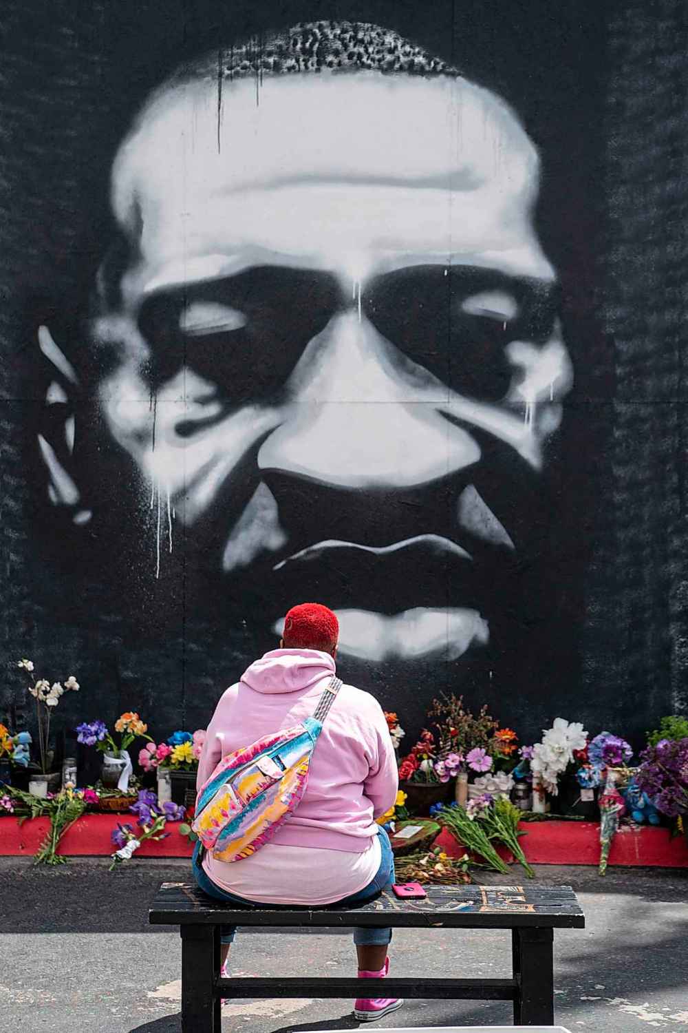 Myisha T. Hall, of Las Vegas, sits on a bench in front of a large mural depicting the late George Floyd, as people from across Minneapolis, and the world gather to visit the George Floyd Memorial Square on Tuesday, May 25, 2021, in Minneapolis, MN. (Kent Nishimura/Los Angeles Times/TNS)