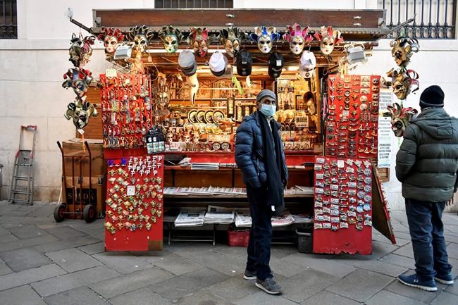 A vendor wearing a face mask stands by a stall in Venice, Italy, Friday, Feb. 28, 2020. Authorities in Italy decided to re-open schools and museums in some of the areas less hard-hit by the coronavirus outbreak in the country which has the most cases outside of Asia, as Italians on Friday yearned for a return to normal life even amid fears that the outbreak could plunge the country's economy into recession. (Claudio Furlan/Lapresse via AP)
