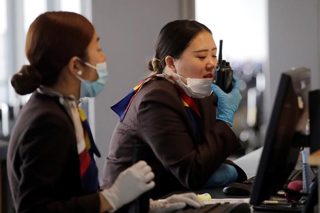A gate agent pulls down her mask to speak on a radio at Seattle-Tacoma International Airport Tuesday, March 3, 2020, in SeaTac, Wash. Six of the 18 Western Washington residents with the coronavirus have died as health officials rush to test more suspected cases and communities brace for spread of the disease. All confirmed cases of the virus in Washington are in Snohomish and King counties. (AP Photo/Elaine Thompson)