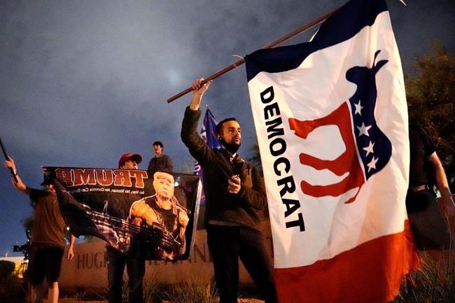 A supporter of Democrat Joe Biden waves a flag near supporters of President Trump in front of the Clark County Election Department, Thursday, Nov. 5, 2020, in Las Vegas. (AP Photo/Jae C. Hong)