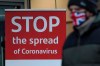 A man wearing a British union flag face mask walks past a coronavirus advice sign outside a bank in Glasgow the morning after stricter lockdown measures came into force for Scotland, Tuesday Jan. 5, 2021. Further measures were put in place Tuesday as part of lockdown restrictions in a bid to halt the spread of the coronavirus.(Andrew Milligan/PA via AP)