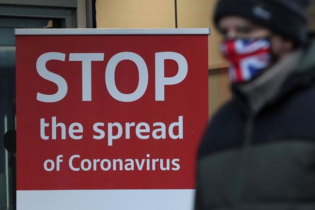 A man wearing a British union flag face mask walks past a coronavirus advice sign outside a bank in Glasgow the morning after stricter lockdown measures came into force for Scotland, Tuesday Jan. 5, 2021. Further measures were put in place Tuesday as part of lockdown restrictions in a bid to halt the spread of the coronavirus.(Andrew Milligan/PA via AP)