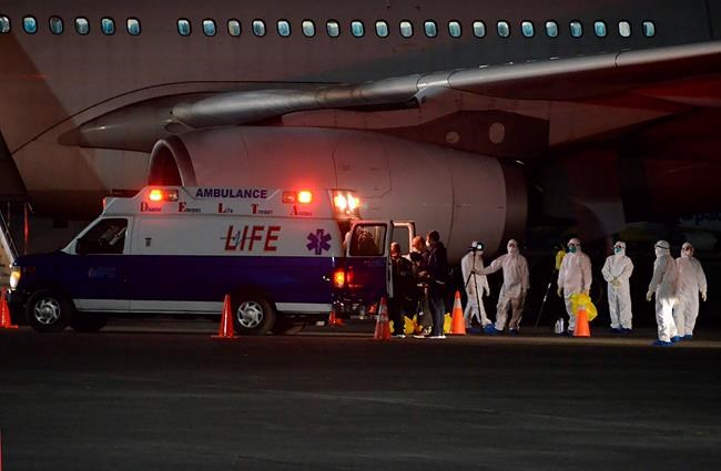 In this handout photo released by Department of Foreign Affairs (DFA), members of the DFA and Department of Health wear protective suits as they assist Filipinos from the Diamond Princess Cruise Ship as they arrive at the Clark airbase, Pampanga, northern Philippines early Wednesday Feb. 26, 2020. Some 445 Filipinos aboard the ship in Japan were flown back to the Philippines on 2 chartered flights. (Department of Foreign Affairs via AP)