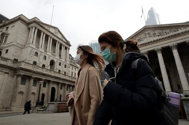 Pedestrians wearing face masks walk past the Bank of England in London, Wednesday, March 11, 2020. Britain's Chancellor of the Exchequer Rishi Sunak will announce the first budget since Britain left the European Union. (AP Photo/Matt Dunham)