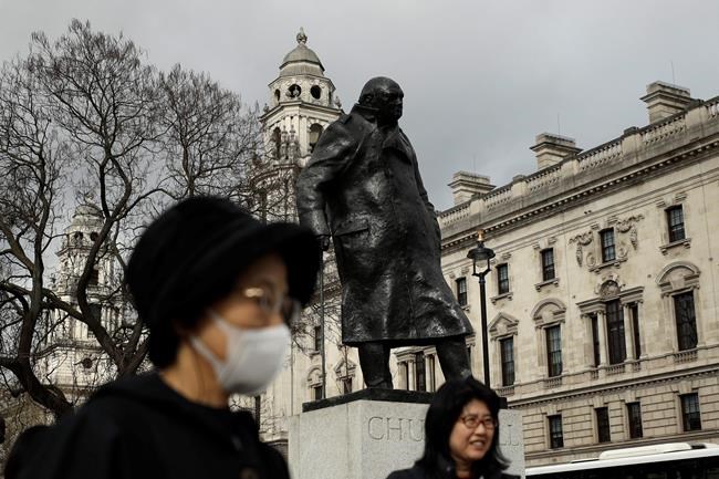 A tourist was a mask to help avoid getting coronavirus as she stands next to the statue of former British Prime Minister Winston Churchill in Parliament Square in London, Wednesday, March 11, 2020. A British government minister Nadine Dorries, who is a junior Heath minster has tested positive for the coronavirus and is self isolating. For most people, the new coronavirus causes only mild or moderate symptoms, such as fever and cough. For some, especially older adults and people with existing health problems, it can cause more severe illness, including pneumonia. (AP Photo/Matt Dunham)