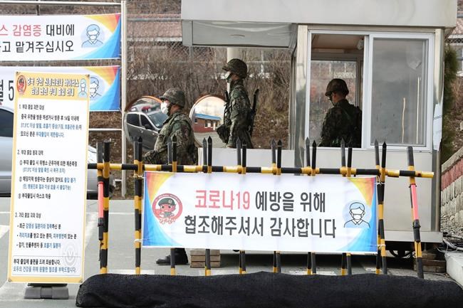 South Korean army soldiers wearing face masks stand guard at a checkpoint of a military base in Daegu, South Korea, Wednesday, Feb. 26, 2020. The number of new virus infections in South Korea jumped again Wednesday and the U.S. military reported its first case among its soldiers based in the Asian country, with his case and many others connected to a southeastern city with an illness cluster. A sign reads