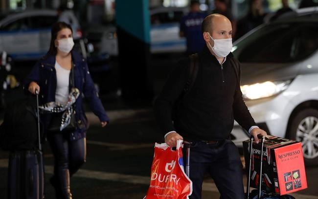 Passengers wearing masks as a precaution against the spread of the new coronavirus COVID-19 arrive to the Sao Paulo International Airport in Sao Paulo, Brazil, Wednesday, Feb. 26, 2020. (AP Photo/Andre Penner)