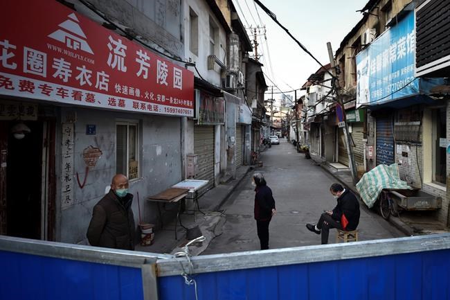 In this Sunday, Feb. 23, 2020, photo, a volunteer sits on a chair keep guard as residents stand near the barricades blocked a residential area in Wuhan in central China's Hubei province Sunday. Warning that China's virus epidemic is