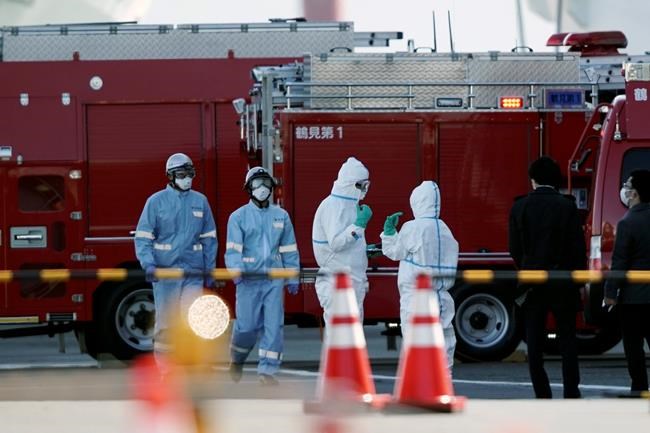 Officials wearing protective suits stand near the cruise ship Diamond Princess at Yokohama Port in Yokohama, south of Tokyo, Thursday, Feb. 6, 2020. Health workers said 10 more people from the Diamond Princess were confirmed ill with the virus, in addition to 10 others who tested positive on Wednesday. They were dropped off as the ship docked and transferred to nearby hospitals for further test and treatment. (AP Photo/Eugene Hoshiko)