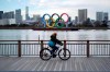A man rides a bicycle near the Olympic rings floating in the water in the Odaiba section Friday, Jan. 8, 2021 in Tokyo. The senior member of the International Olympic Committee has said he “can’t be certain”the postponed Tokyo Olympics will open in just over six months because of the surging pandemic in Japan and elsewhere. (AP Photo/Eugene Hoshiko)