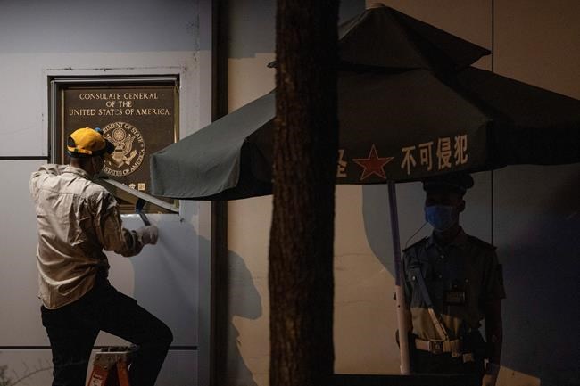 A worker tries to remove the plaque from the United States Consulate near a Chinese paramilitary policeman on guard in Chengdu in southwest China's Sichuan province on Sunday, July 26, 2020. The ongoing sharp deterioration in U.S.-China ties poses risks to both countries and the rest of the world. In the latest escalation, a U.S. consulate in Chengdu in southwestern China shuttered Monday, ordered by China to close in retaliation for the U.S. shutting down its consulate in Houston last week. (AP Photo/Ng Han Guan)