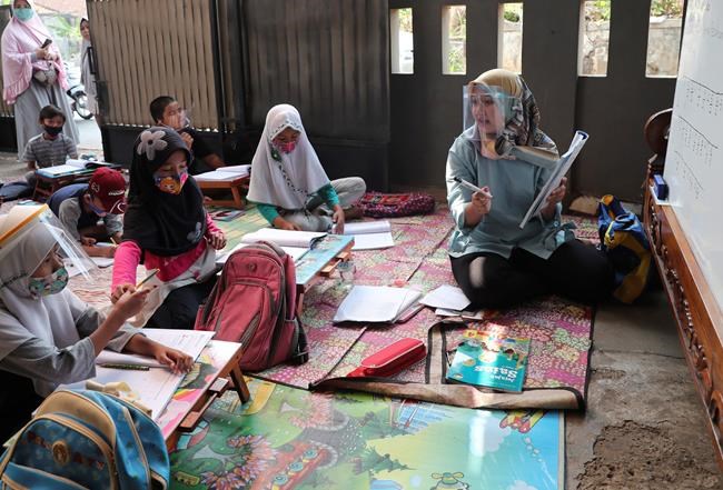 Teacher Inggit Andini, right, wearing a face shield as a precaution against the new coronavirus outbreak, speaks as her students in a makeshift classroom at her residence in Tangerang, Indonesia, Monday, Aug. 10, 2020. Andini offered free extra lessons for students who lack access to the internet as the school where she works at remain closed and switched to online learning due to the outbreak. (AP Photo/Tatan Syuflana)