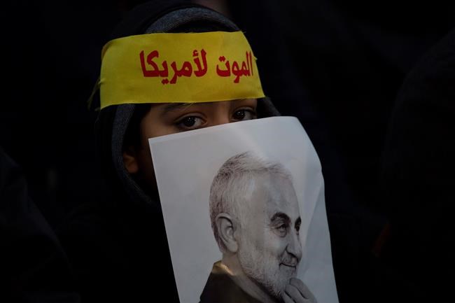 A child peeks from behind a picture of slain Iranian Revolutionary Guard Gen. Qassem Soleimani as supporters of Hezbollah leader Sayyed Hassan Nasrallah gather for his televised speech in a southern suburb of Beirut, Lebanon, Sunday, Jan. 5, 2020 following the U.S. airstrike in Iraq that killed Soleimani. The headband reads,