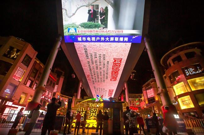 People watch a large screen showing President Donald Trump and First Lady Melania Trump during a news report from Chinese state television about Trump testing positive for the coronavirus in Beijing, Friday, Oct. 2, 2020. Trump said early Friday that he and first lady Melania Trump have tested positive for the coronavirus, a stunning announcement that plunges the country deeper into uncertainty just a month before the presidential election. (AP Photo/Mark Schiefelbein)