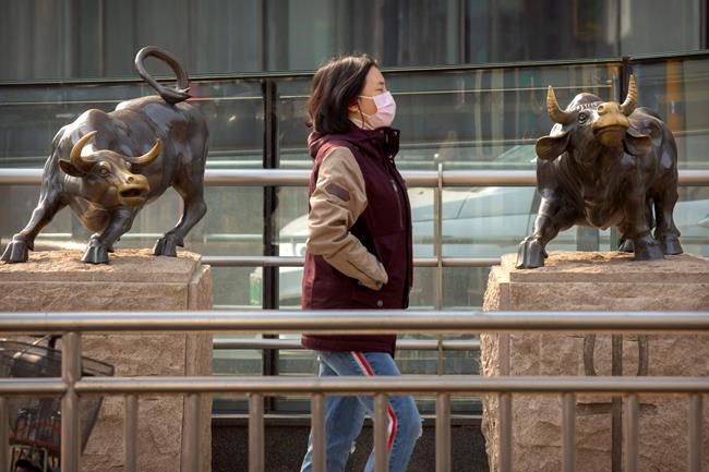 A woman wearing a face mask walks past statues of bulls in Beijing, Friday, Feb. 28, 2020. Asian stock markets fell further Friday on spreading virus fears, deepening an global rout after Wall Street endured its biggest one-day drop in nine years. (AP Photo/Mark Schiefelbein)