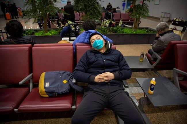 A traveler wears a face mask as he naps at Beijing Capital International Airport in Beijing, Thursday, Jan. 23, 2020. China closed off a city of more than 11 million people Thursday in an unprecedented effort to try to contain a deadly new viral illness that has sickened hundreds and spread to other cities and countries in the Lunar New Year travel rush. (AP Photo/Mark Schiefelbein)