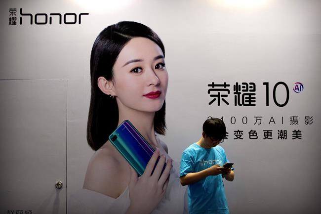 A staff member uses his smartphone in front of a billboard for Chinese smartphone brand Honor at the Global Mobile Internet Conference in Beijing on April 26, 2018. In an announcement Tuesday, Nov. 17, 2020, Chinese tech giant Huawei says it is selling its budget-price Honor smartphone brand in an effort to rescue the struggling business from damaging U.S. sanctions imposed on its parent company. (AP Photo/Mark Schiefelbein)