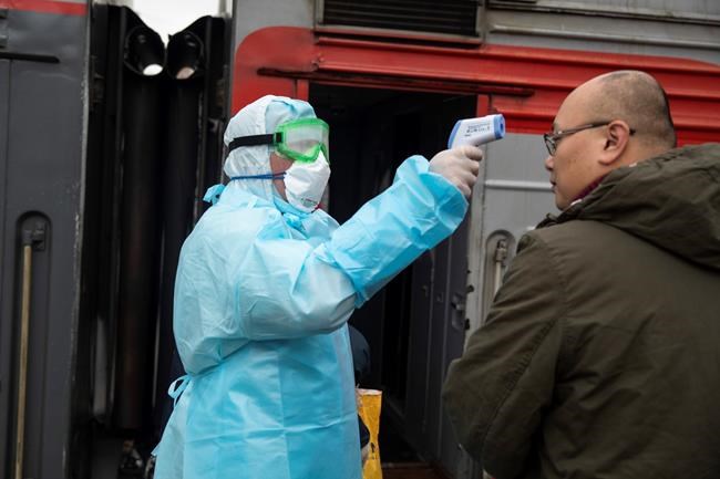 A medical worker in a hazardous materials suit uses a body thermal scanner to check temperature of Chinese passenger who just arrived from Beijing at the Yaroslavsky railway station in Moscow, Russia, Friday, Jan. 31, 2020. Russia has reported the first two cases of a new virus in the country. (AP Photo/Pavel Golovkin)