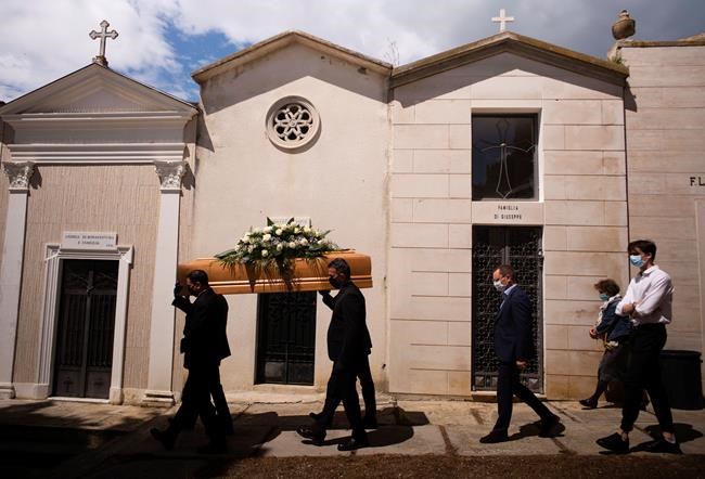 FILE - In this May 12, 2020 file photo, the casket containing the body of Annunziata Ginoble, the mother of Mayor of Roseto degli Abruzzi Sabatino Di Girolamo, third from right, with his sister, Marisa Di Felice, second from right, and his son, Francesco, right, is taken to her burial site inside the small cemetery of Montepagano, central Italy. Italy is poised to reclaim the dishonor of reporting the most coronavirus deaths in Europe, as the second surge ravages the country’s disproportionately old population and exposes how public health shortfalls and delayed restrictions compounded a lack of preparedness going into the pandemic. (AP Photo/Domenico Stinellis, file)