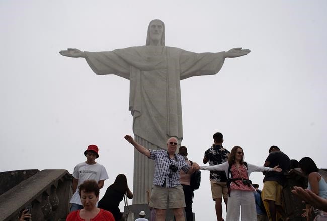 Tourists pose for photos in front of the Christ the Redeemer statue in a foggy day in Rio de Janeiro, Brazil, Tuesday, March 17, 2020. The company that administers transport and installations at Rio's Sugarloaf Mountain, another postcard destination that sees 1.5 million visitors annually, said it is closing shop on Tuesday for 15 days as a measure to prevent the spread of the new coronavirus. (AP Photo/Silvia Izquierdo)