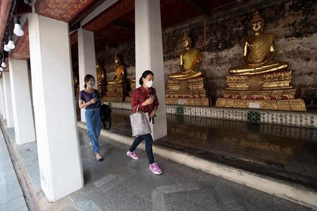 People wear face masks to protect from a new coronavirus walk in front of Buddha statues at Suthat Temple in Bangkok, Thailand, Tuesday, March 10, 2020. For most people, the new coronavirus causes only mild or moderate symptoms, such as fever and cough. For some, especially older adults and people with existing health problems, it can cause more severe illness, including pneumonia. (AP Photo/Sakchai Lalit)