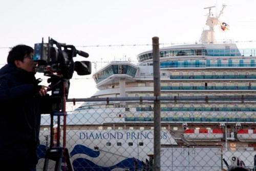A TV cameraman films the quarantined ship Diamond Princess, background, anchored at Yokohama port in Yokohama, near Tokyo, Tuesday, Feb. 18, 2020. The cruise ship will begin letting passengers off the boat on Wednesday after it’s been in quarantined for 14 days. (AP Photo/Koji Sasahara)
