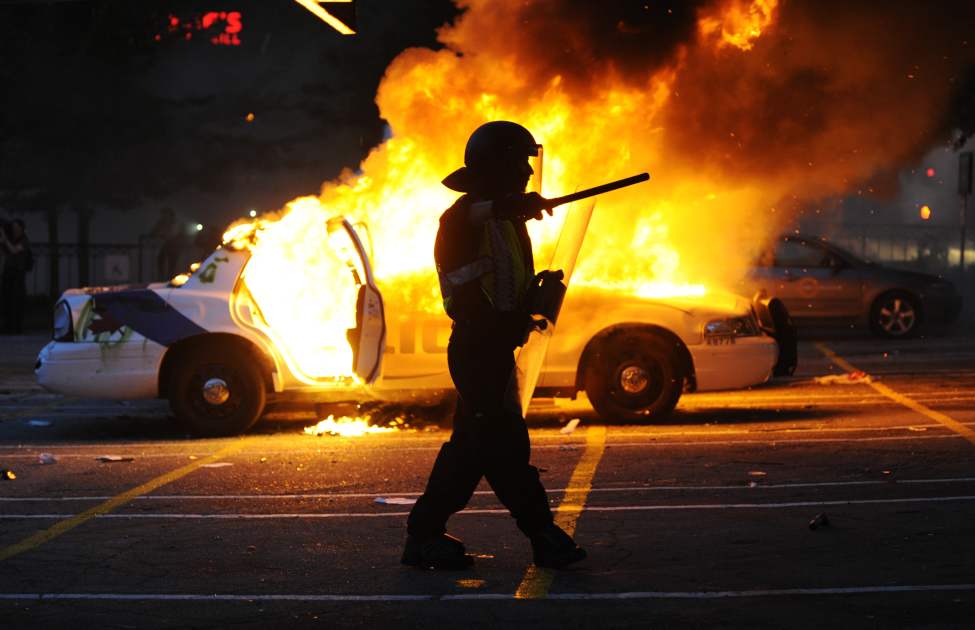 A police riot officer gestures to the crowd as he walks past two burning police cars set on fire by Canucks fans after the Vancouver Canucks lost to the Boston Bruins in the Stanley Cup Final, Vancouver, June 15 2011. ( Gerry Kahrmann / PNG staff photo)