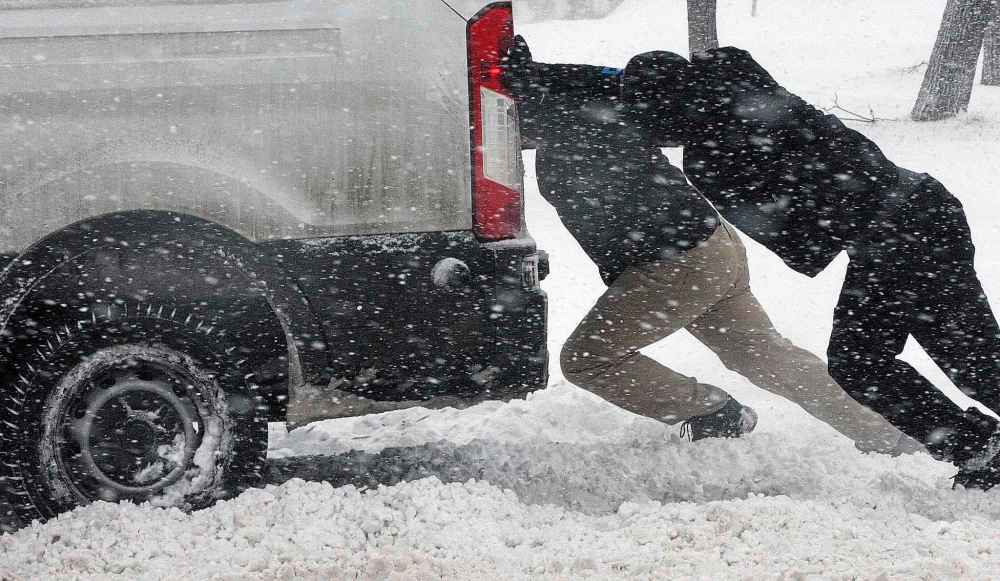 Cameron Batista (front) and others help to push out a delivery van stuck in snow on Ellice Avenue during a winter storm in December 2016.