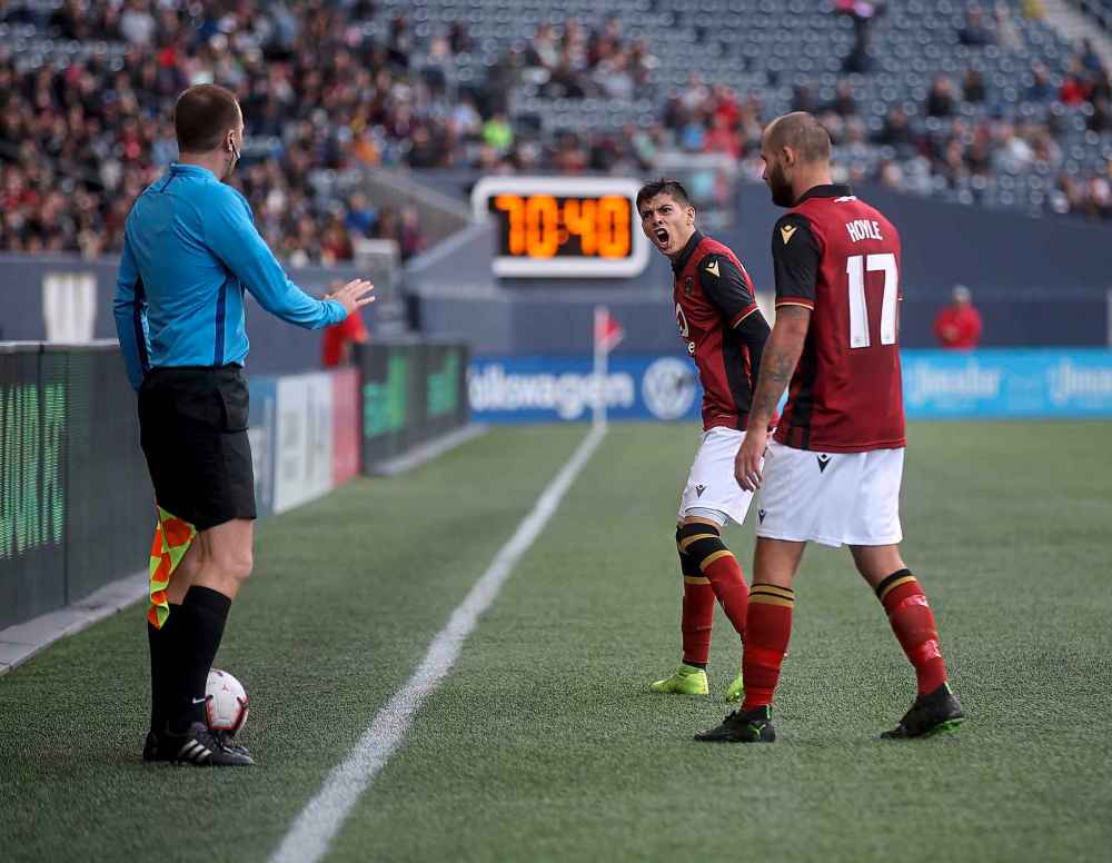 Valour FC's Diego Gutierrez (centre) and Stephen Hoyle (right) argue with an official before Gutierrez is shown a yellow card.
