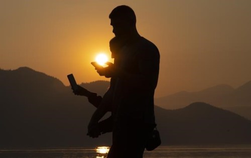 A couple are silhouetted against the smoke filled sky as they both look on their smart phones in Britannia Beach, B.C., Friday, October 2, 2020. Ontario's right to disconnect policy comes into effect today.THE CANADIAN PRESS/Jonathan Hayward