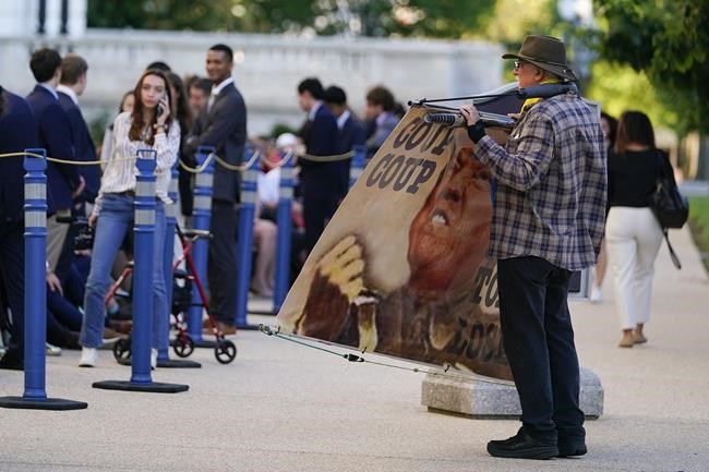 An activist holds a sign next to a line of people waiting to enter the Cannon Building, Thursday, June 9, 2022, in Washington. The House select committee will have its first public hearing in its investigation of the Jan. 6 attack on the U.S. Capitol. The hearing is expected to reveal the findings of a year-long investigation. (AP Photo/Julio Cortez)