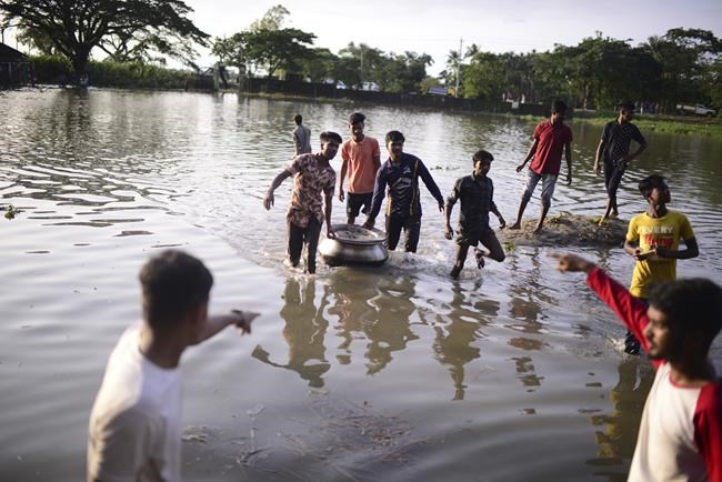 People walk through flood waters in Sunamganj, Bangladesh, Tuesday, June 21, 2022. Villagers in northeastern Bangladesh are crowding makeshift refugee centers and scrambling to meet boats arriving with food and fresh water as massive floods, which have killed dozens of people and displaced hundreds of thousands. (AP Photo/Mahmud Hossain Opu)