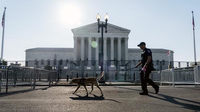 A Police officer leads a K9 around steel fencing and barricades surrounding the Supreme Court, Friday, June 24, 2022, in Washington. (AP Photo/Gemunu Amarasinghe)