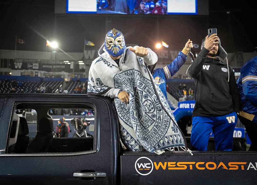 Bombers player Sergio Castillo (in mask) joins teammates in a truck bed as it circles IG Field. (Jessica Lee / Winnipeg Free Press)