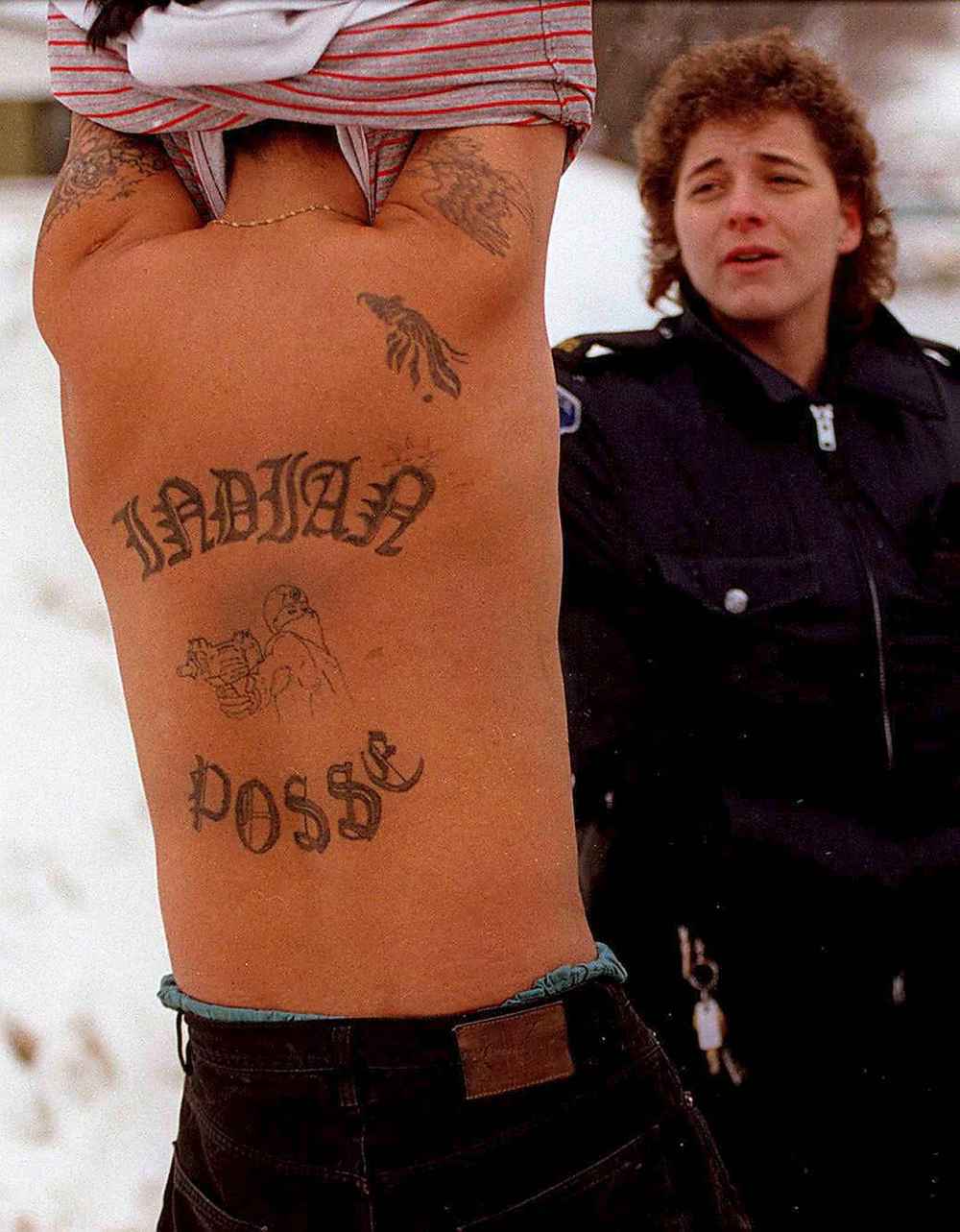 A gang member wanted by police shows an officer he is not armed -- revealing a huge gang tattoo -- before being taken into custody in 1997.