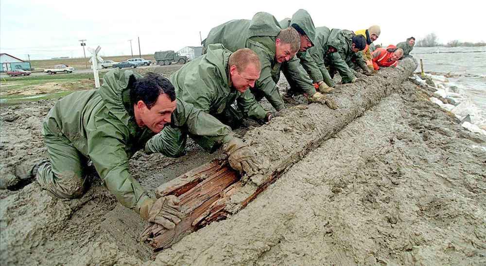 Members of Calgary's 1st Battalion, Princess Patricia's Canadian Light Infantry battle 80 km/hour winds to push logs and sandbags to create a breakwater to help protect the town of St. Jean Baptise's dike from rising floodwaters in 1997.