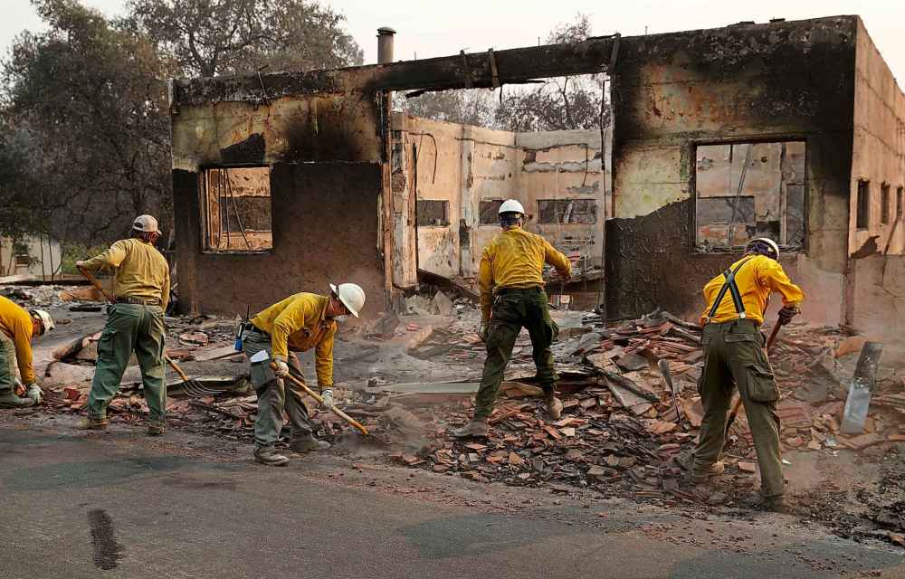 Fire crews clear rubble from the road near a building burned Monday in Paradise, Calif. (John Locher / The Associated Press)