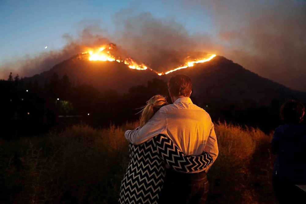 Roger Bloxberg and his wife Anne hug as they watch a wildfire on a hill near their home Friday in West Hills, Calif. (Marcio Jose Sanchez / The Associated Press)