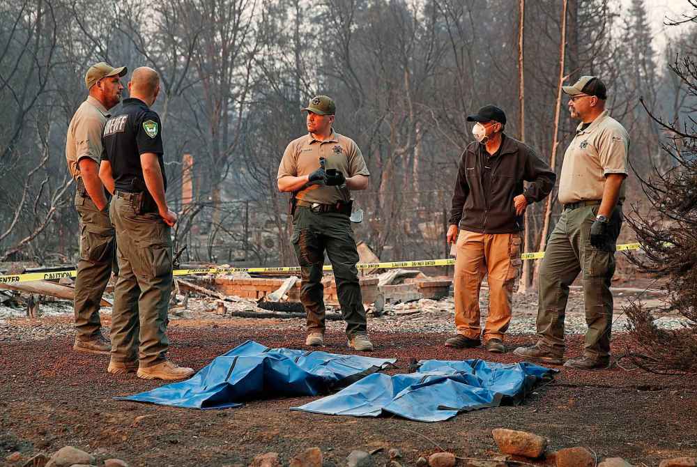 Officials stand over human remains at a burned out home destroyed Sunday in Paradise, Calif. (John Locher / The Associated Press)