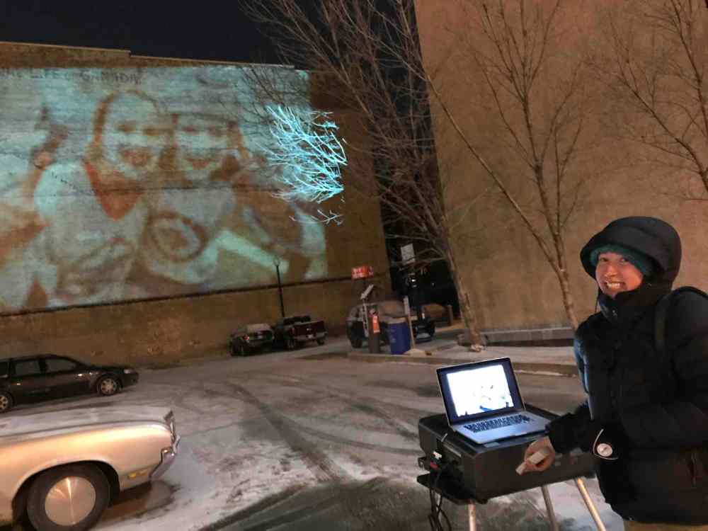 Free Press photojournalist Mikaela MacKenzie bundled up in the unseasonably cold weather Thursday while running the projector.