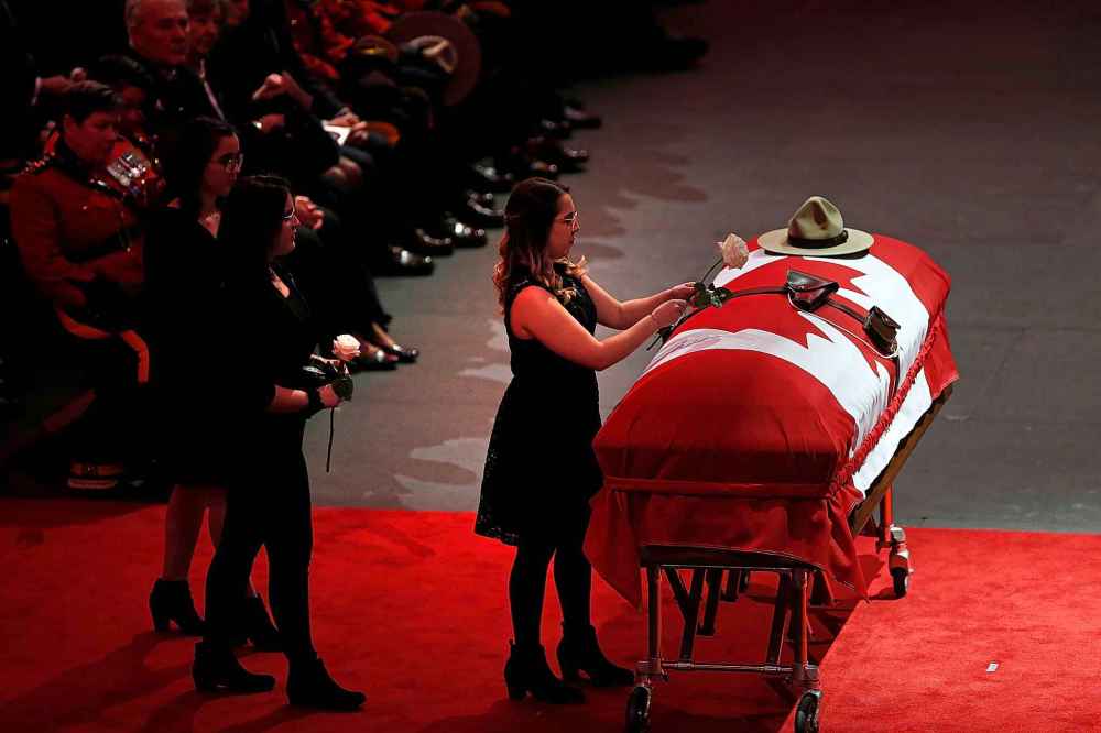 The daughters of RCMP Constable Allan Poapst, Krystal, Chelsie and Caitlyn, place flowers on the casket. (John Woods / The Canadian Press)