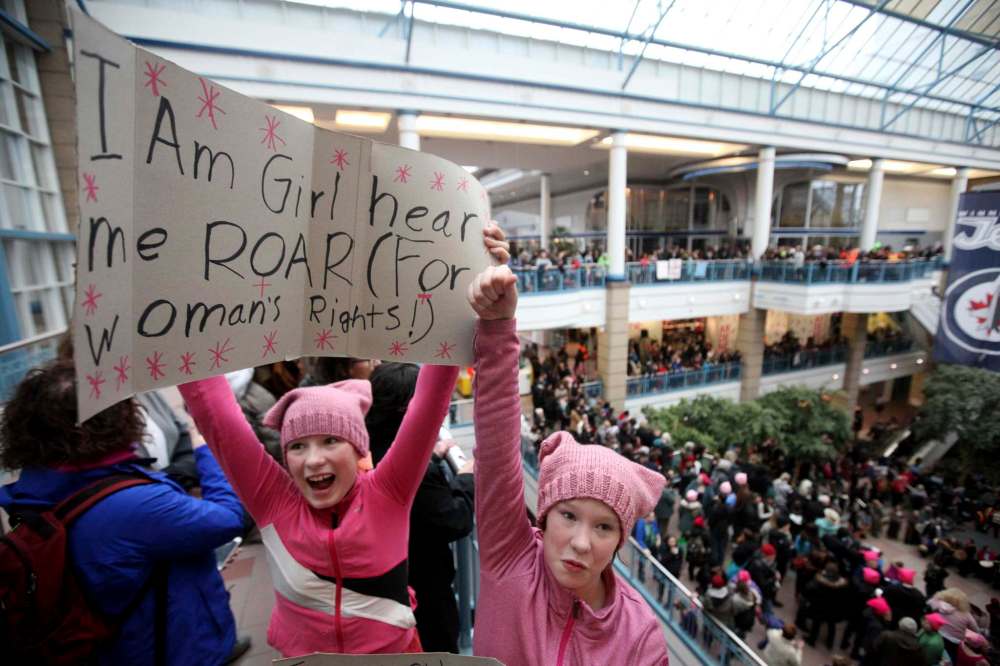 10-year-old twins Fiona (left) and Ruby hold signs and join thousands of others at Portage Place during the Women's Day rally and march, Saturday.