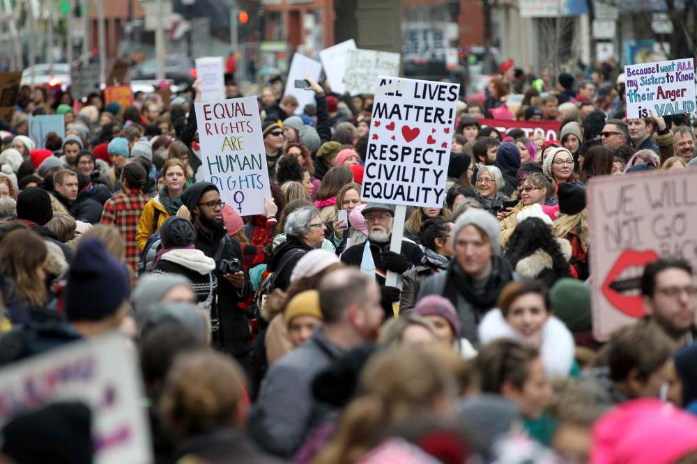Protest signs are raised by the hundreds as marchers make their way down Portage Ave. Saturday.