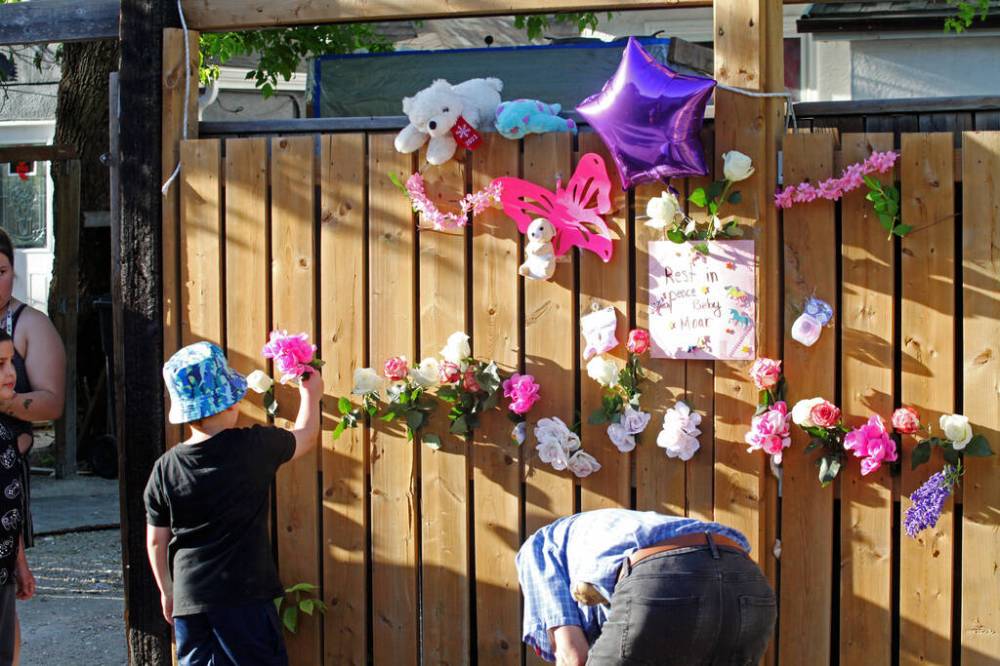 ERIK PINDERA/WINNIPEG FREE PRESS FILES
A child places a flower into the fence at the vigil in the alley behind Boyd Avenue for an unnamed baby that was found dead in a garbage bin last month. The baby’s mother is now charged with manslaughter.