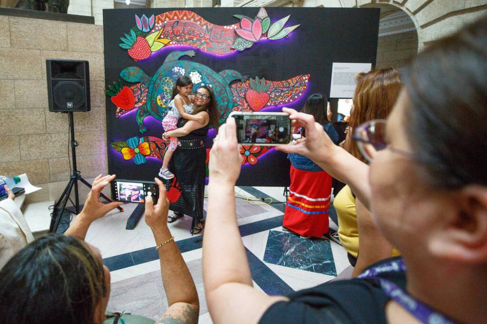 MIKE DEAL / WINNIPEG FREE PRESS
Renowned local Indigenous artist Jackie Traverse holds Sophia Edwards, 5, in front of the work of art she produced with Indigenous youth and the Clan Mothers elders.