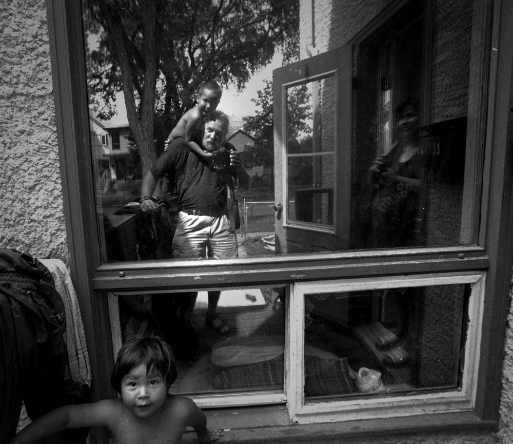 August 2001: Captured in a window's reflection, Margaret, a single mom expecting her seventh child, watches as Jamie climbs onto Hossack's shoulders. The family was part of a Free Press series on child poverty.