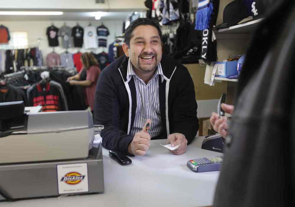 Mohamed El tassi, one of the owners of Sargent Blue Jeans, jokes with customers while at the till in his store at the neighbourhood Jean store on Sargent Avenue.