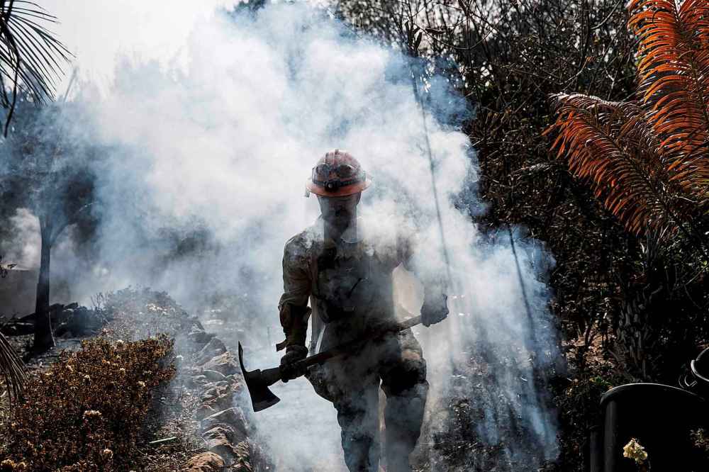 LA County firefighter Battalion 13 Captain Victor Correa helps put out hotspot in a neighbourhood razed by the Woolsey fire on Harvester road in Malibu, Calif. Monday. (Marcus Yam / Los Angeles Times)