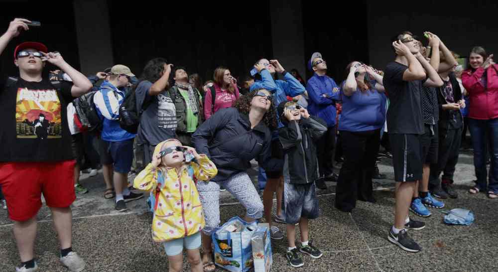 A gathering outside the Manitoba Museum get glimpses of the partial eclipse through clouds Monday. (Wayne Glowacki / Winnipeg Free Press)