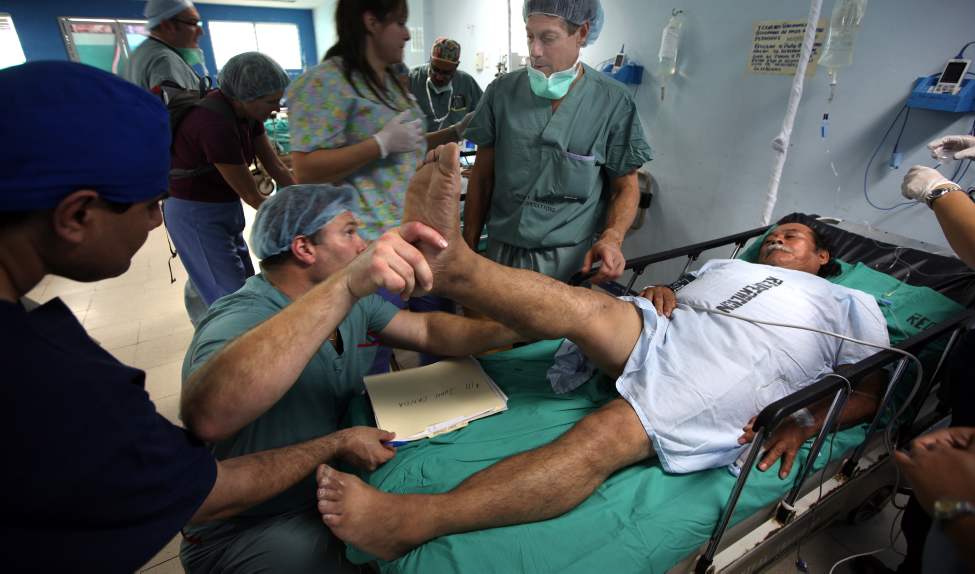 Prior to the first operation Dr. Jason Crosby lifts Juan Canda's leg as Dr. Hedden watches.